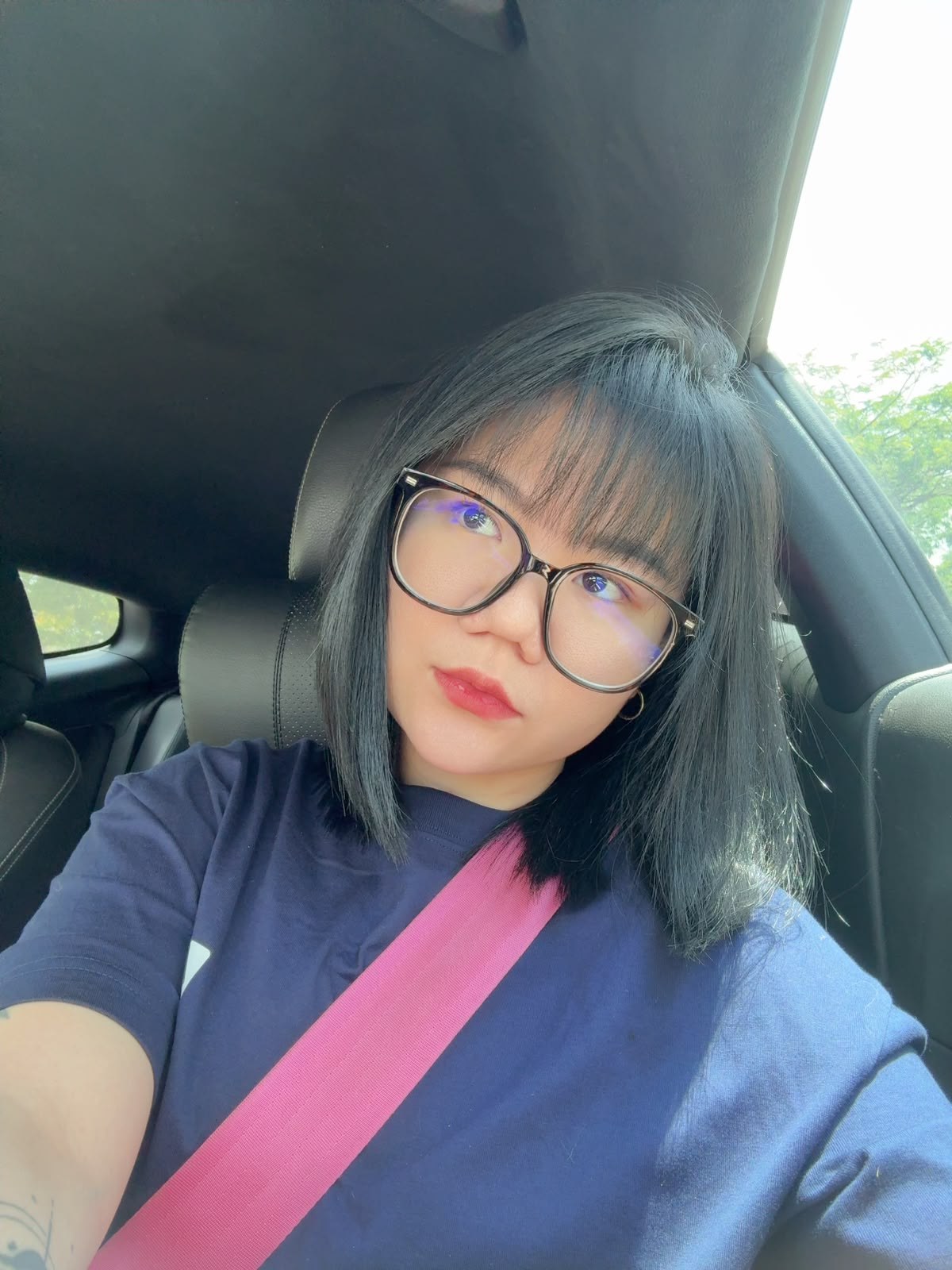 Faye wearing glasses and a pink seat belt in a car