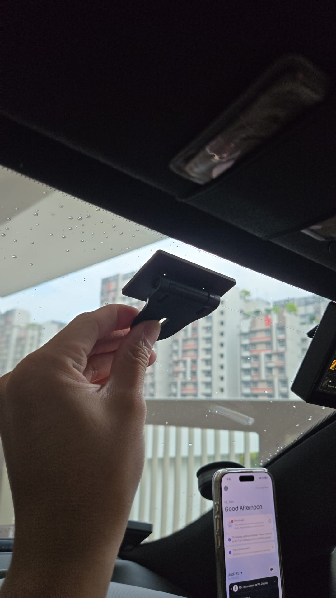Rear view of the black PD-Display mount held near a car windscreen, showing the flat mounting plate and bracket.